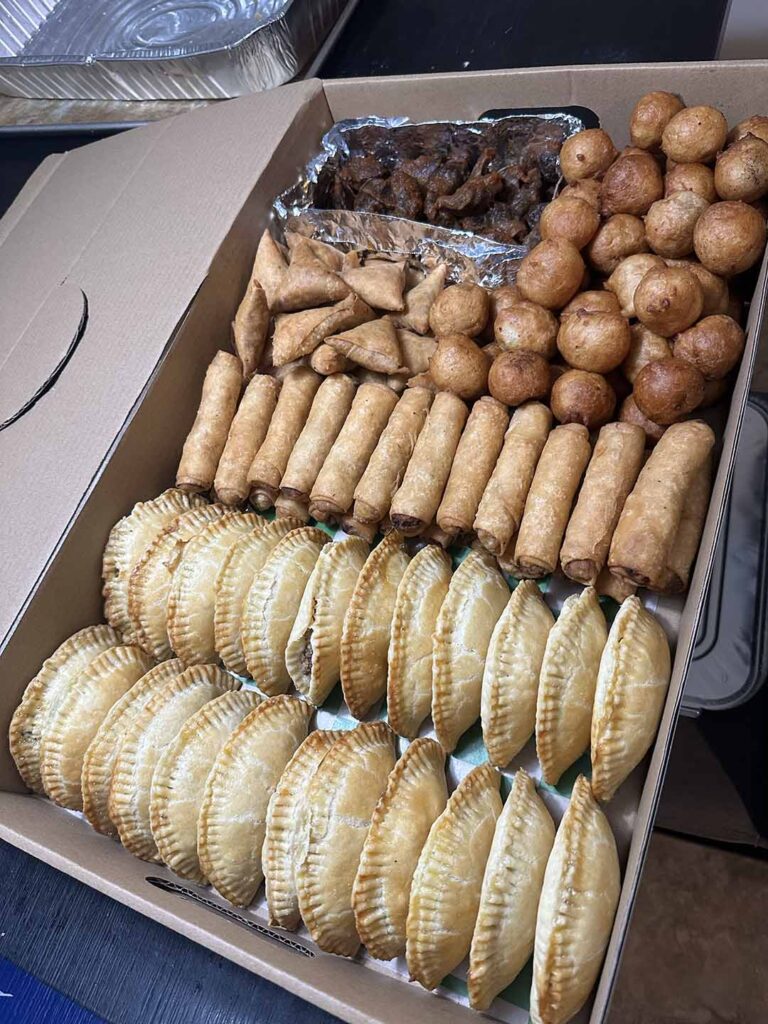 A box combo of Nigerian finger foods, namely: meat pies, springrolls, samosas, puff puffs, and peppered gizzards.